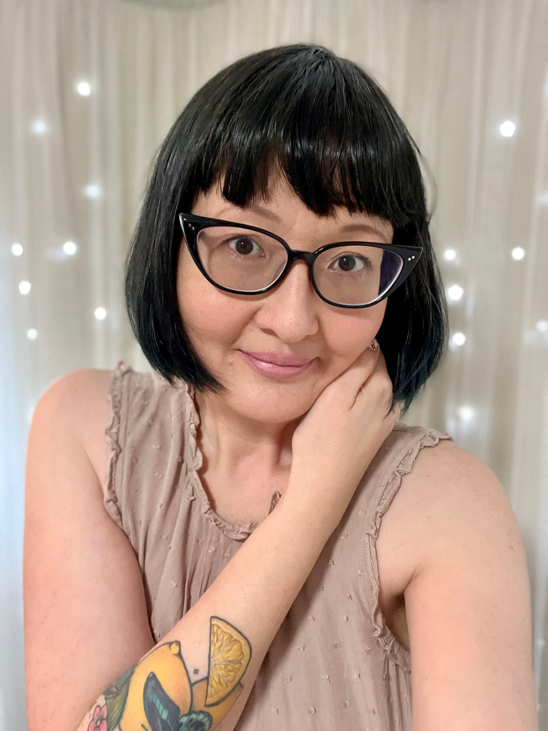 An image of me, Kat Kruger, with short black hair and bangs. I have black-rimmed cats eye glasses and am wearing a beige sleeveless top.